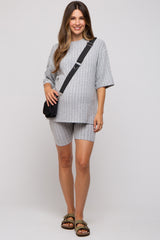 woman wearing a gray ribbed maternity short set with a loose top and shorts, holding a small bag and standing confidently