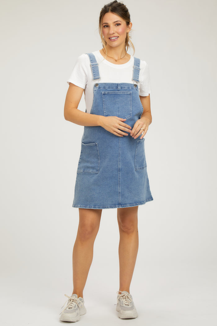 woman wearing a light blue denim maternity overall dress and holding her baby bump