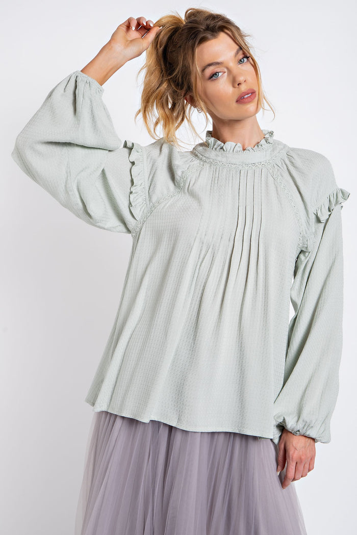 woman wearing a light green long sleeve ruffled blouse with pleating detail and puff sleeves, paired with a tulle skirt