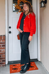 woman wearing a bright red fluffy maternity cardigan and black flared jeans, holding her baby bump by the front door
