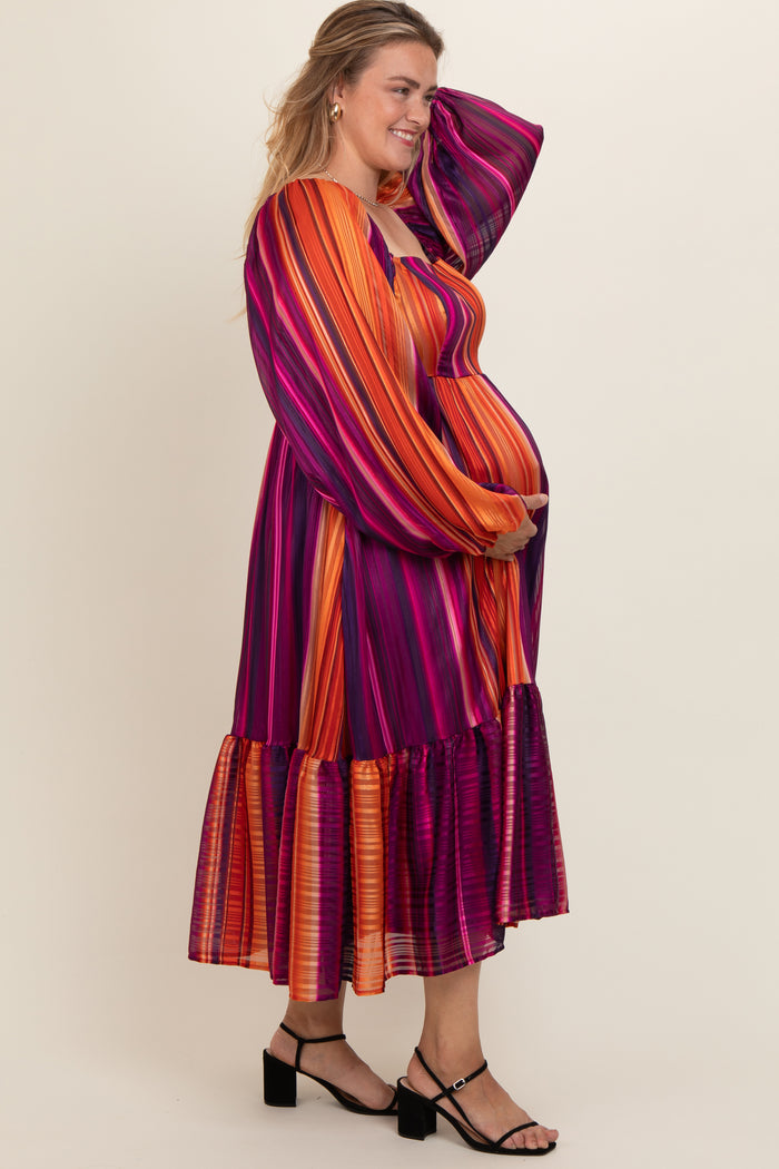 woman wearing a multicolored striped maternity dress with long sleeves and a ruffled hem, holding her baby bump