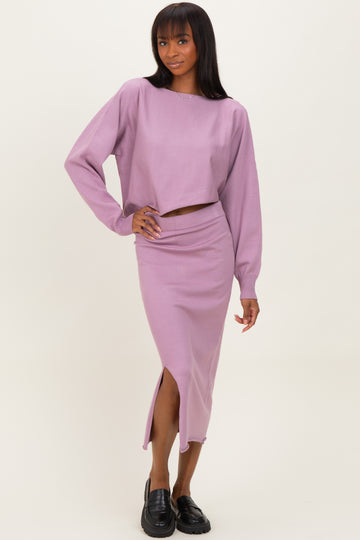 woman wearing a lavender two-piece set consisting of a cropped long sleeve top and a matching midi skirt with a slit