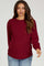 woman wearing a burgundy maternity sweater with a round neckline and long sleeves, paired with light blue jeans