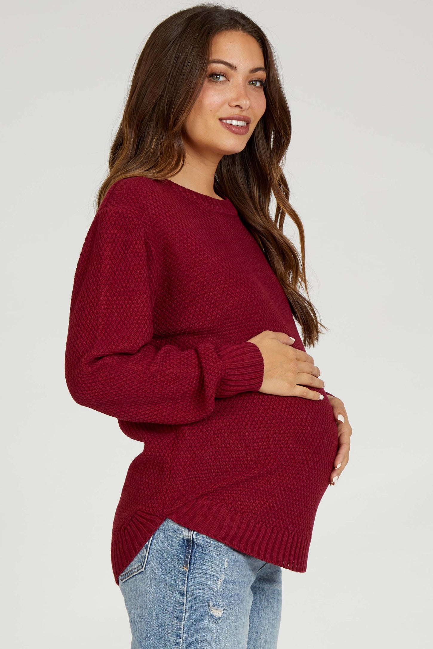 woman wearing a burgundy maternity sweater with a relaxed fit and holding her baby bump