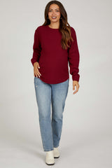 woman wearing a burgundy knitted maternity sweater paired with light blue straight leg jeans and beige ankle boots