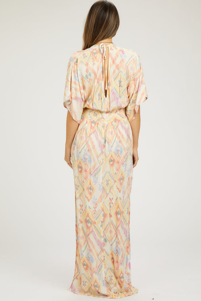 woman wearing a pastel patterned maternity maxi dress with short sleeves and a tie at the neck.