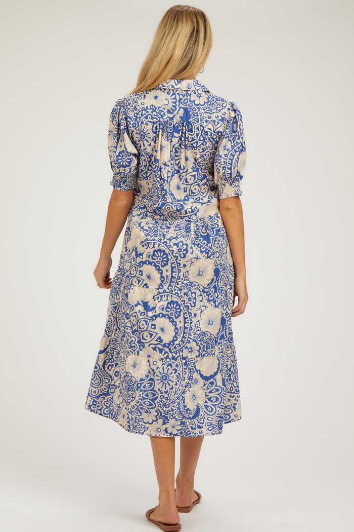 woman wearing a blue and cream floral printed maternity midi dress with puff sleeves and a tie detail at the back