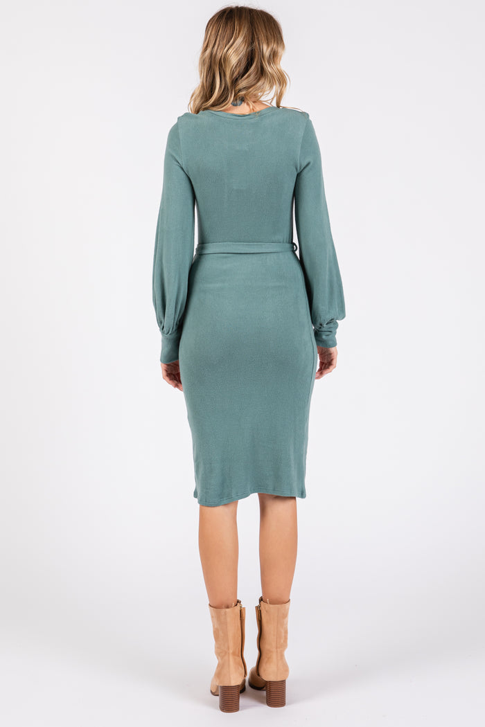 woman wearing a green long sleeve fitted dress with a waist tie and ankle boots, viewed from the back