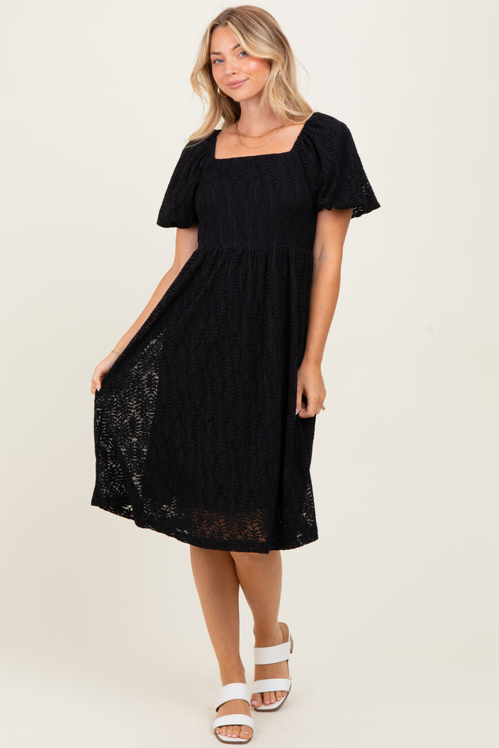 woman wearing a black short sleeve square neck midi dress with a lace overlay and a-flowy skirt