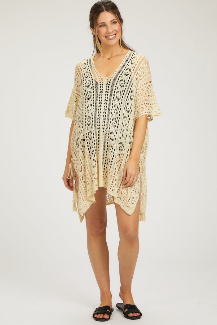 woman wearing a cream crochet maternity cover-up with a v-neck and side ties, showcasing her baby bump