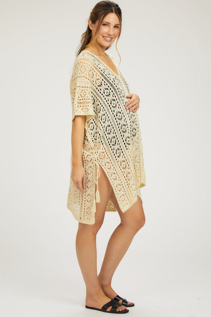 woman wearing a beige crochet cover-up maternity wear with side ties and holding her baby bump