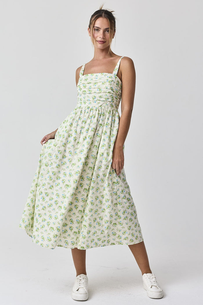 woman wearing a floral midi dress with adjustable straps and a smocked bodice, paired with white sneakers
