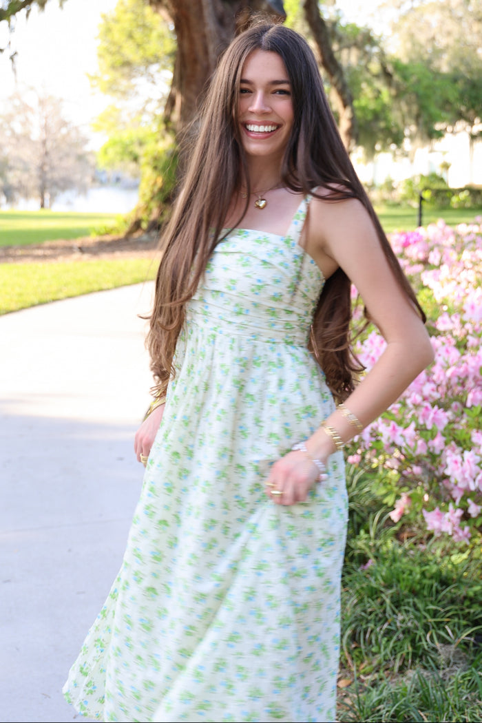 woman wearing a light green floral maxi dress with spaghetti straps and smiling outdoors