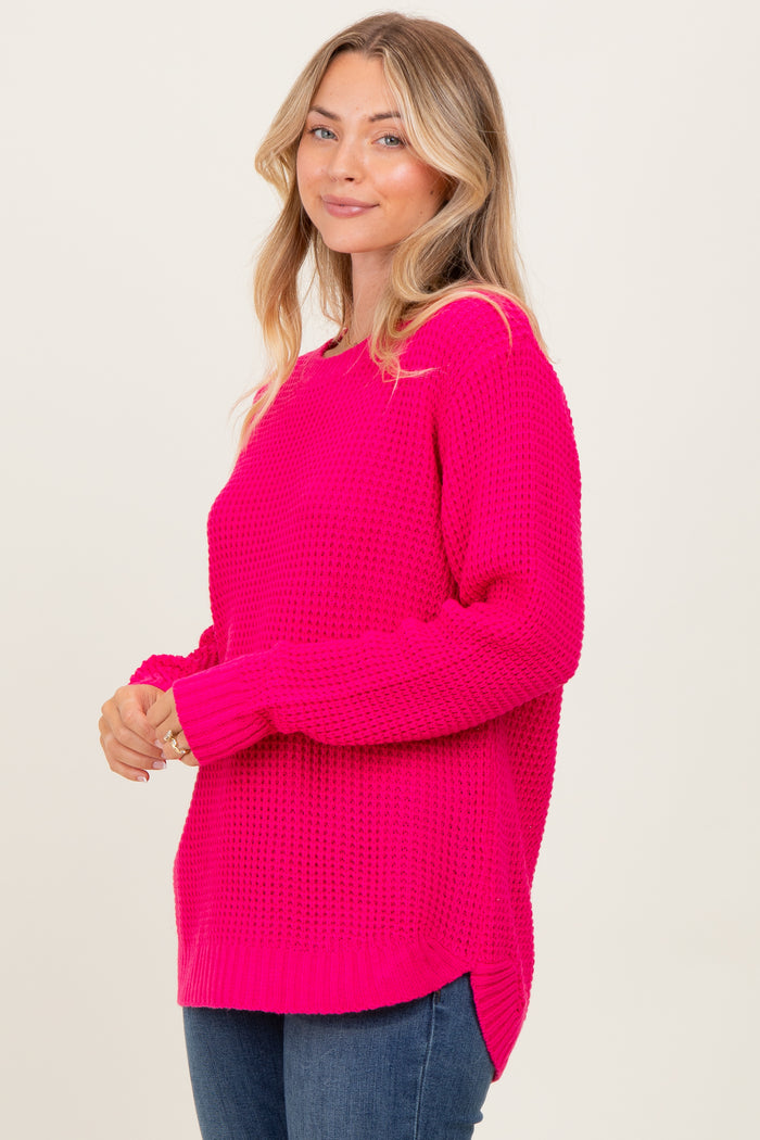 woman wearing a bright pink oversized knitted sweater with side slits and long sleeves, styled with blue jeans
