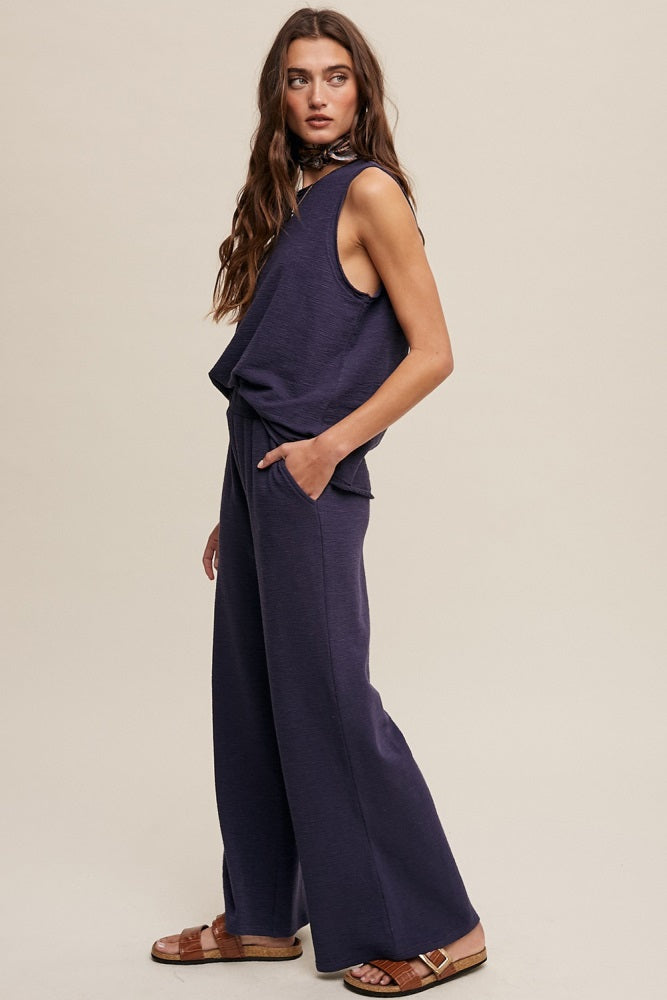 woman wearing a dark purple sleeveless top and wide-leg pants with pockets, standing sideways against a neutral background