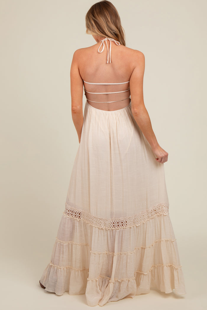 woman wearing a cream-colored maternity maxi dress with a halter neck and tiered ruffle details on the skirt
