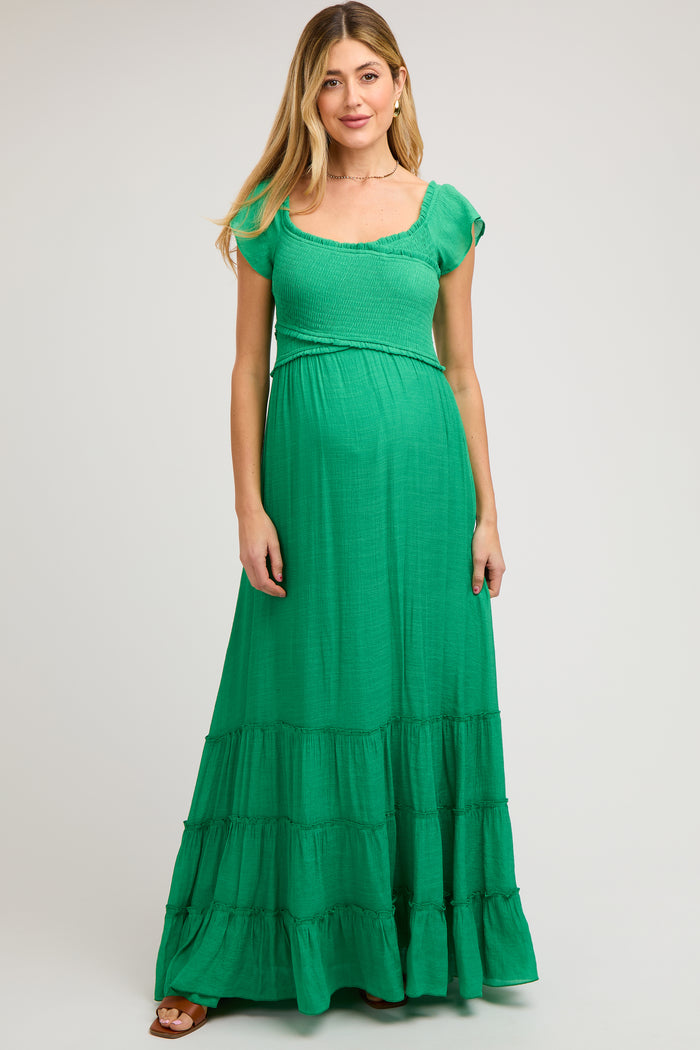 woman wearing a green maxi maternity dress with short sleeves and tiered skirt, showcasing a baby bump