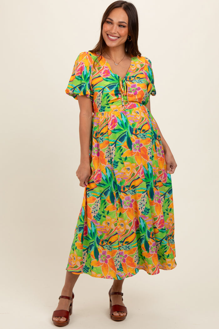 woman wearing a vibrant floral maternity dress with short sleeves and a tie detail, showcasing her baby bump