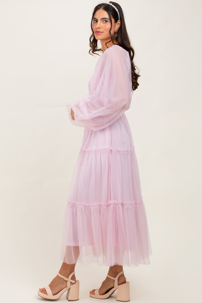 woman wearing a flowy pink midi dress with tiered tulle layers and long sheer sleeves