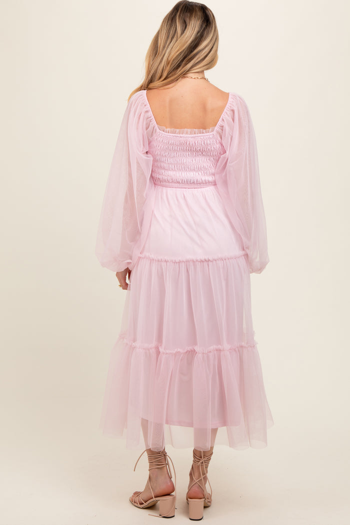 woman wearing a pink maternity dress with puff sleeves and tiered skirt, showing a smocked back detail