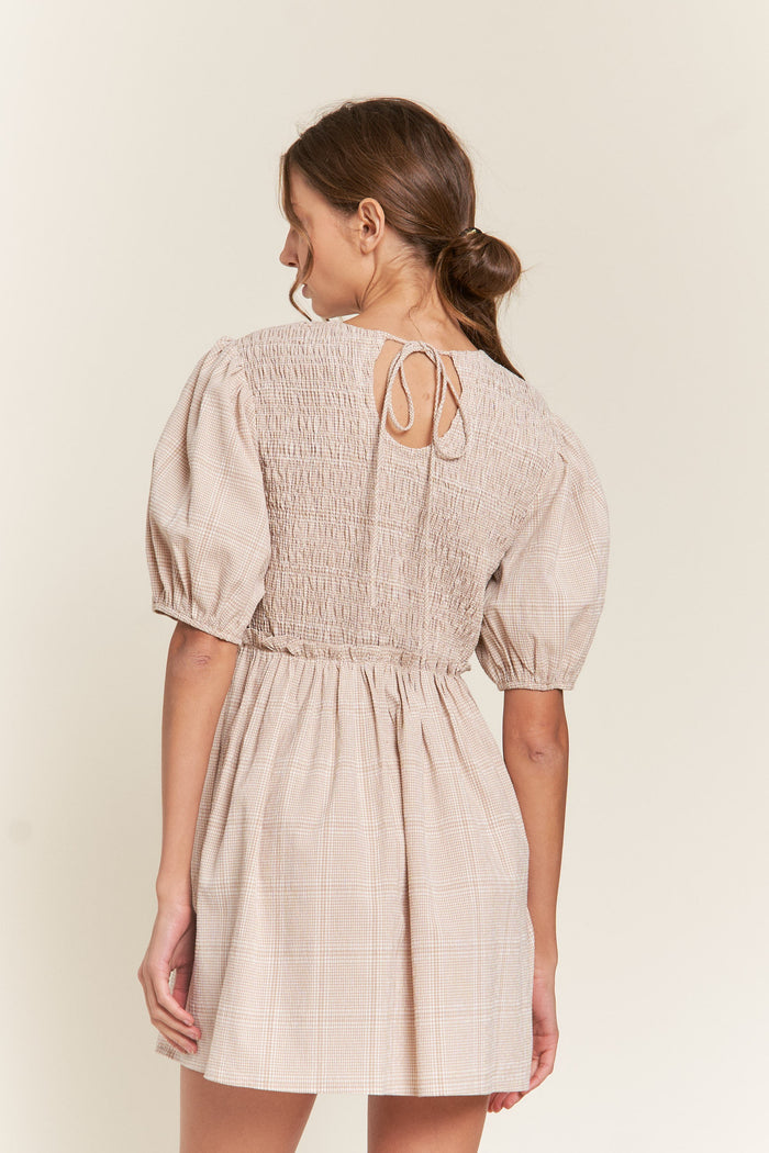 woman wearing a beige checkered smocked mini dress with puff sleeves and a tie closure at the back