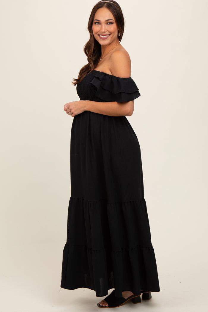 woman wearing a black off-the-shoulder maternity maxi dress with ruffled sleeves and tiered skirt, showing her baby bump