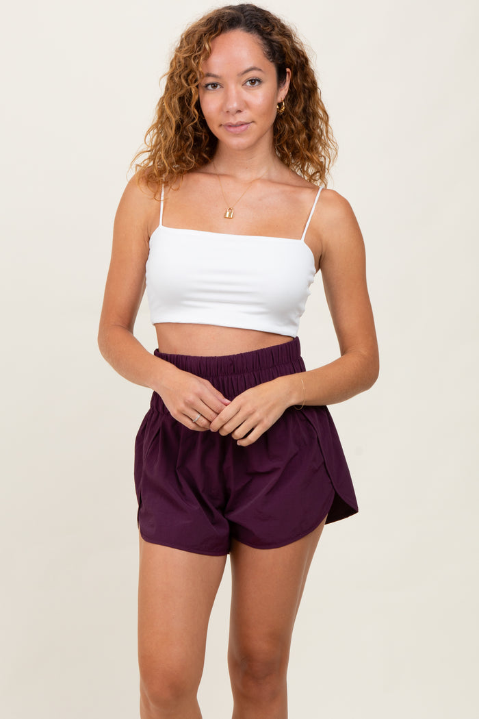 woman wearing a white cropped tank top and high-waisted maroon shorts with an elastic waistband