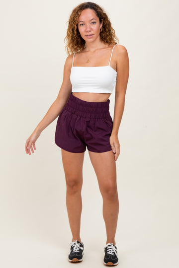 woman wearing a white crop top and purple elastic waist shorts with a relaxed fit