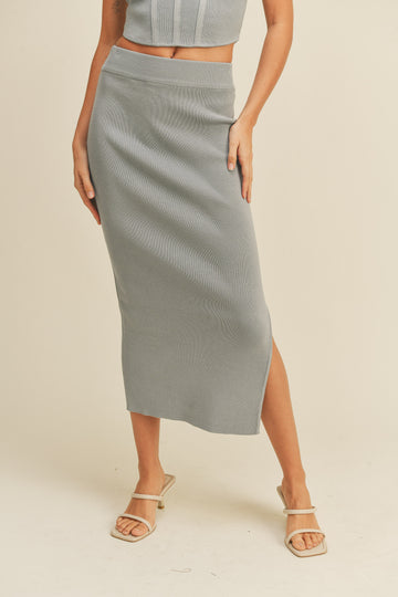 woman wearing a light gray ribbed midi skirt with a side slit and matching crop top