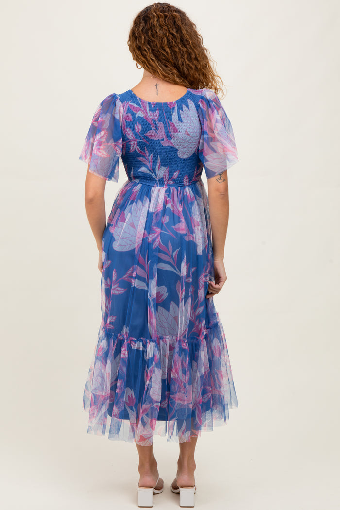 woman wearing a sheer blue floral maxi dress with puff sleeves and a ruffled hem, seen from the back