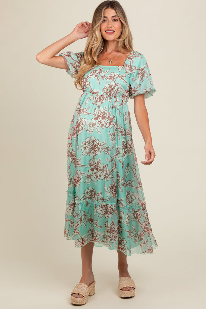 woman wearing a mint green floral maternity dress with short sleeves and a tiered skirt, showing her baby bump