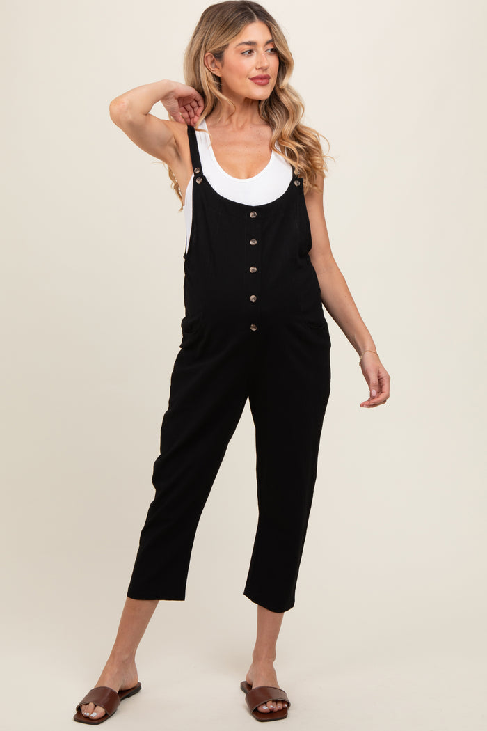 woman wearing a black maternity overall jumpsuit with buttons and pockets, showing off her baby bump
