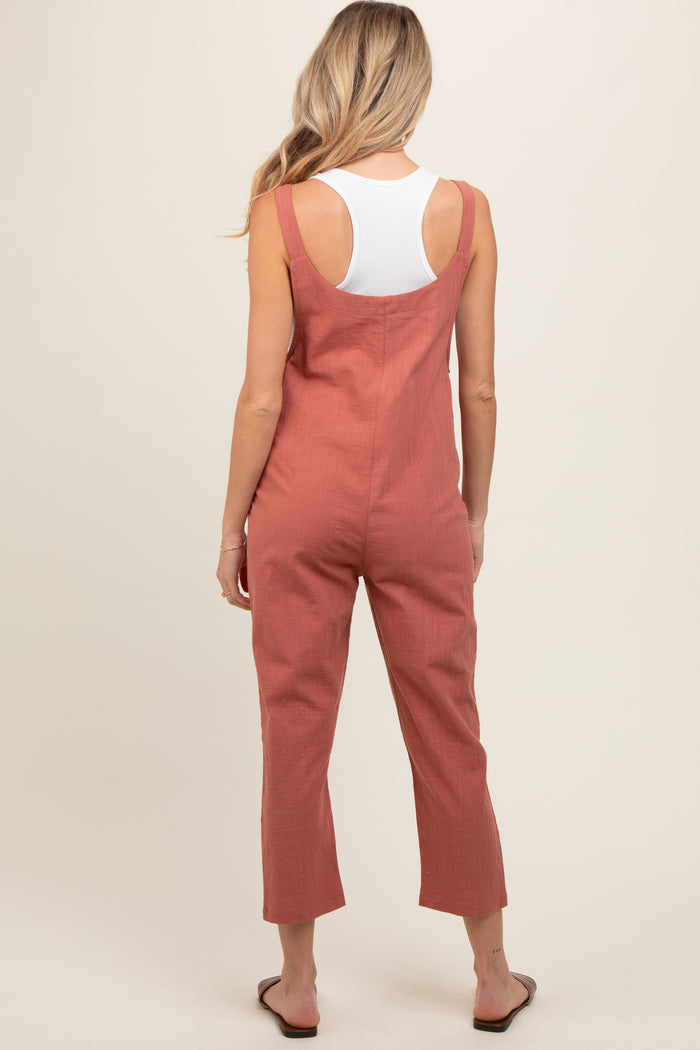 woman wearing a rust-colored maternity jumpsuit with wide legs and adjustable straps, shown from the back