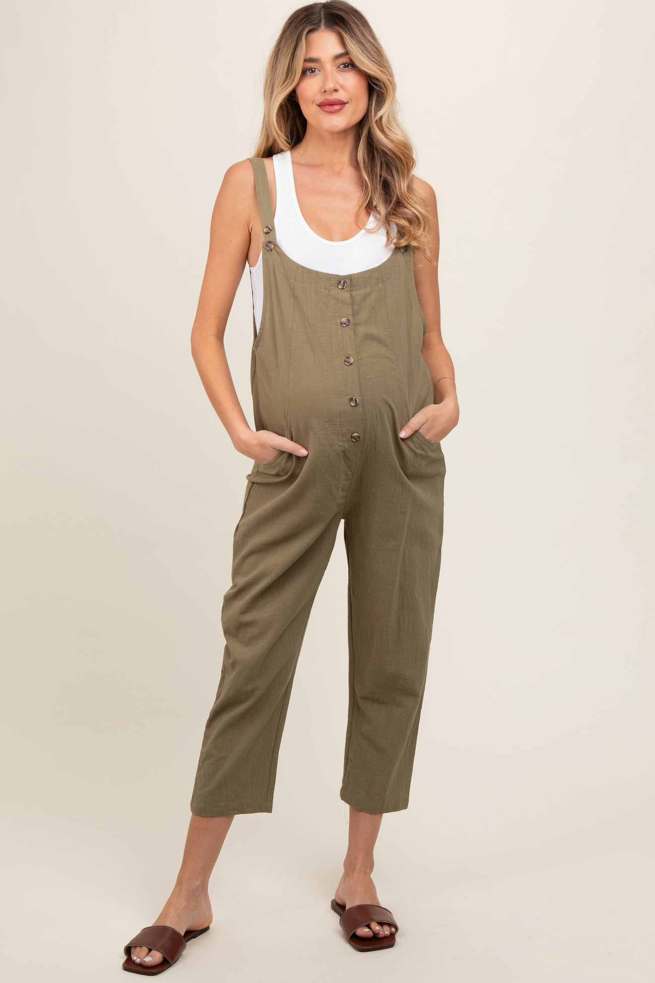 woman wearing a light olive green maternity jumpsuit with buttons and side pockets, showing her baby bump