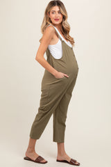 woman wearing a green maternity jumpsuit with buttons and pockets, showcasing her baby bump