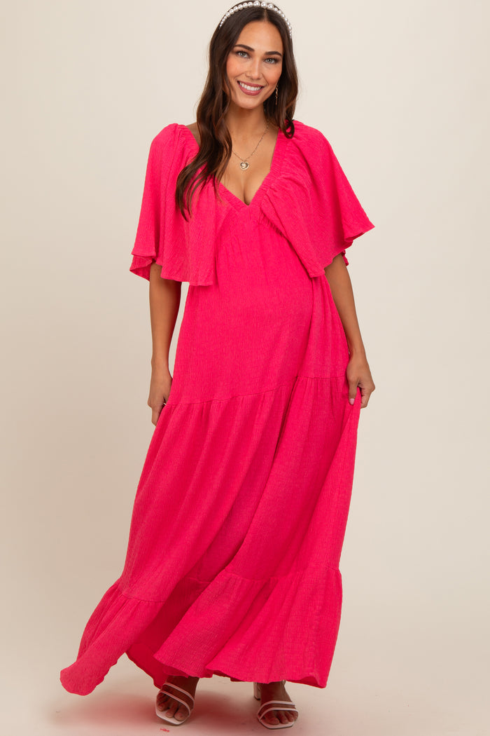 woman wearing a bright pink maternity maxi dress with flutter sleeves and a flowy skirt, showing her baby bump