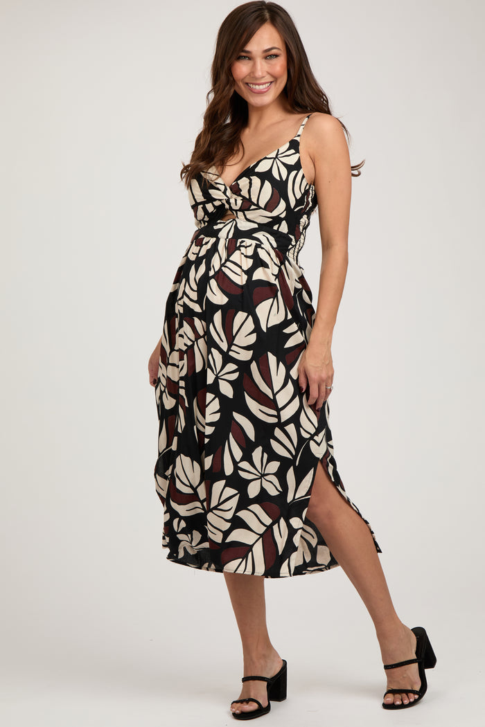woman wearing a black and cream floral maternity dress with a knot detail and side slits, showing her baby bump