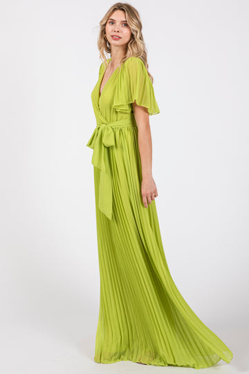 woman wearing a bright green pleated maxi dress with flutter sleeves and a tie waist