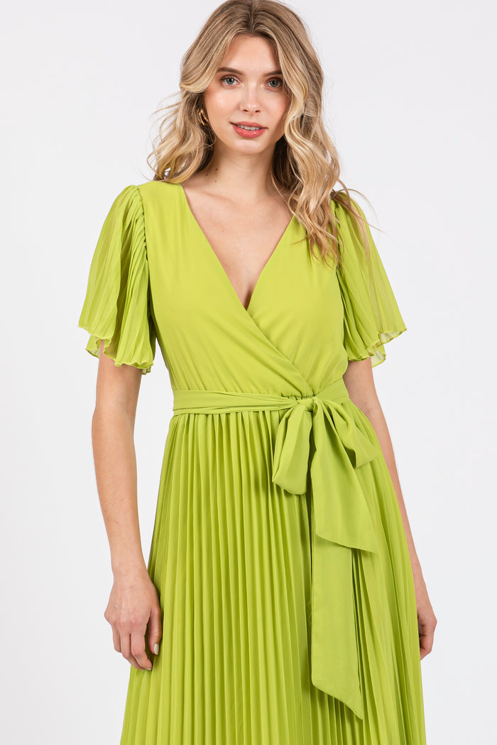 woman wearing a vibrant green pleated wrap dress with short sleeves and a belted waist