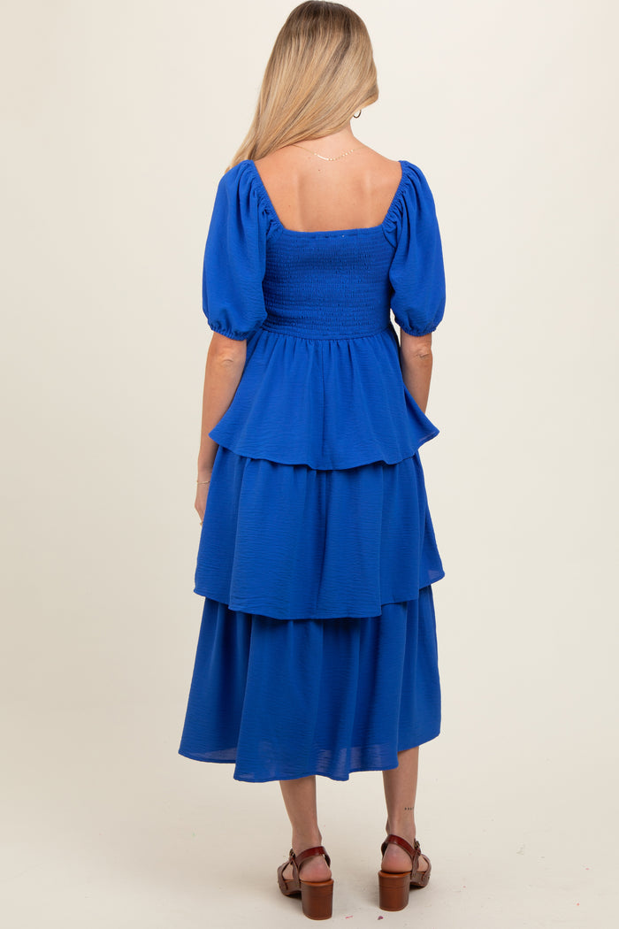 woman wearing a blue maternity dress with puff sleeves and tiered ruffles, showing a relaxed fit from the back