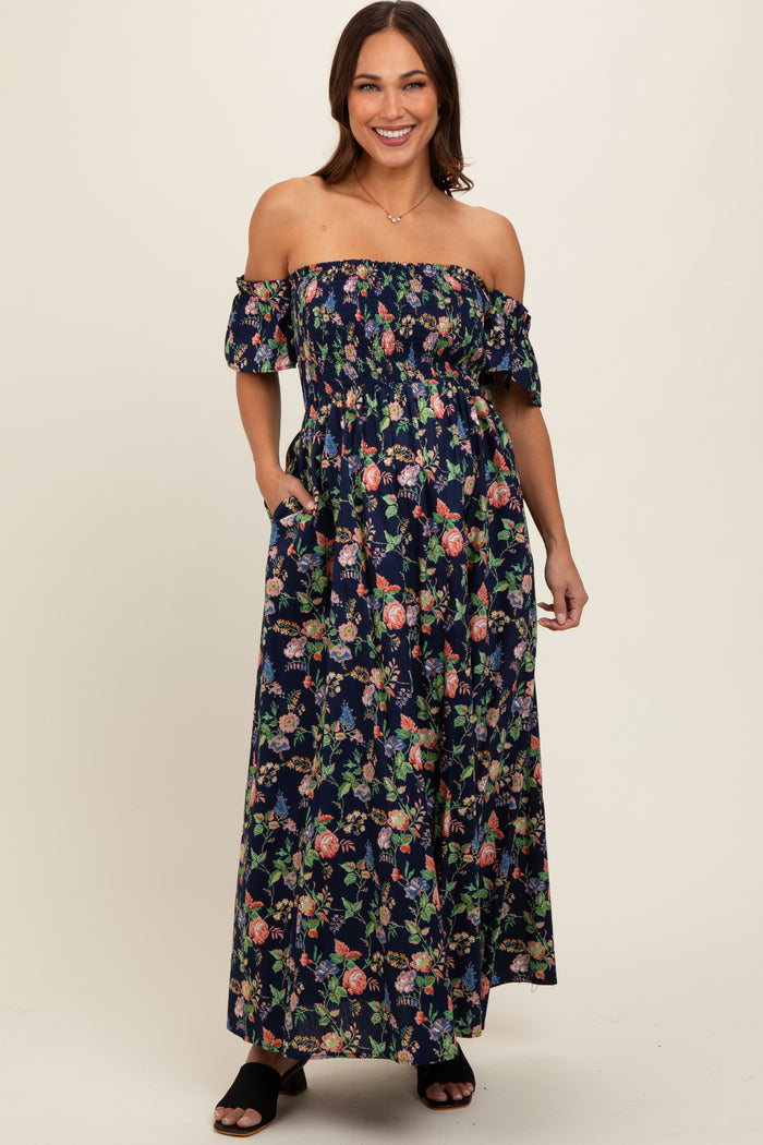 woman wearing a navy floral off-shoulder maternity maxi dress with pockets and a fitted bodice, displaying a baby bump