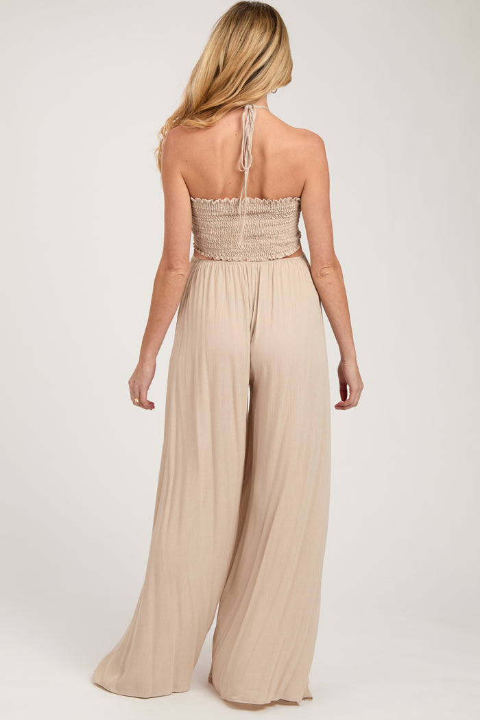 woman wearing a tan maternity jumpsuit with a smocked bodice and wide leg pants, showing her back
