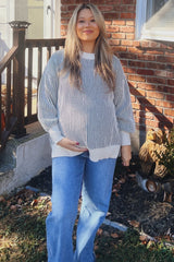 woman wearing a cream and grey striped maternity sweater and blue flared jeans, showing her baby bump
