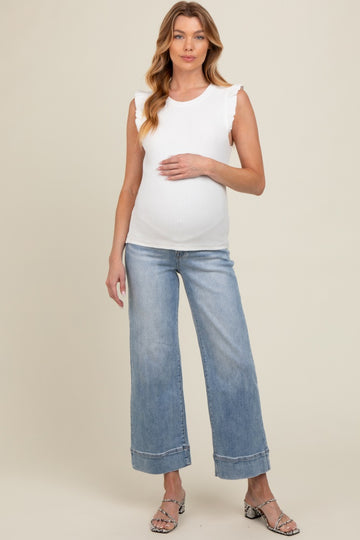 woman wearing a white sleeveless maternity top with ruffle details and light blue wide-leg maternity jeans, showcasing her baby bump