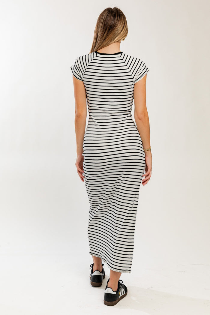 woman wearing a black and white striped maxi dress, viewed from the back, with short cap sleeves and fitted silhouette