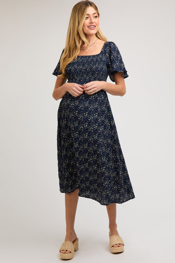 woman wearing a navy floral maternity dress with short sleeves and a square neckline, highlighting her baby bump
