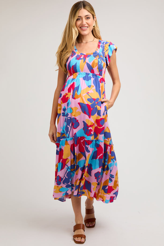 woman wearing a colorful floral maternity dress with ruffled sleeves and tiered skirt, showing her baby bump