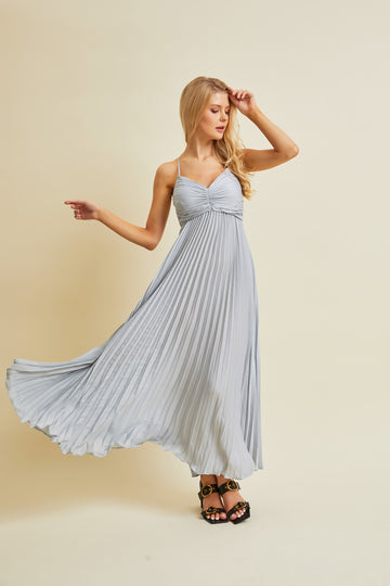 woman wearing a light blue pleated maxi dress with spaghetti straps, spinning gracefully in the dress
