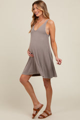 woman wearing a taupe sleeveless maternity dress and holding her baby bump