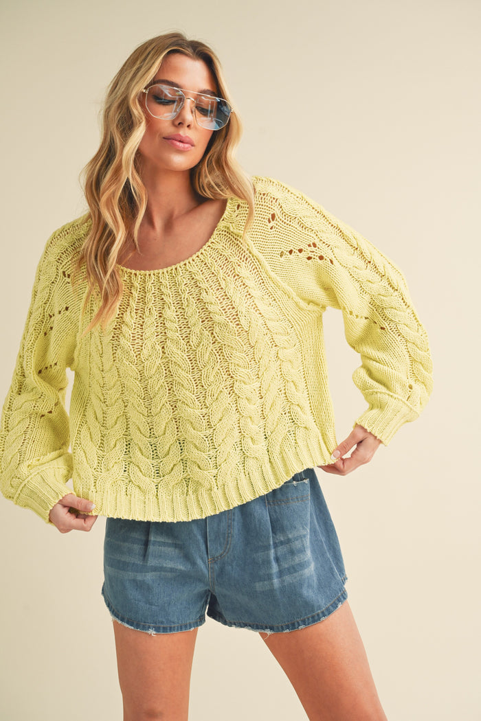 woman wearing a bright yellow cable knit sweater with a scoop neckline and loose fit, paired with denim shorts